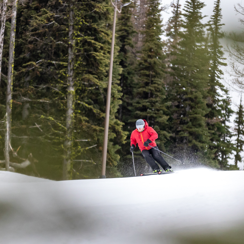 Red jacket skier on groomer through trees