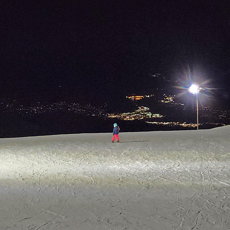 Young skier at the top of Mission Ridge at night looking out over the valley filled with lights.