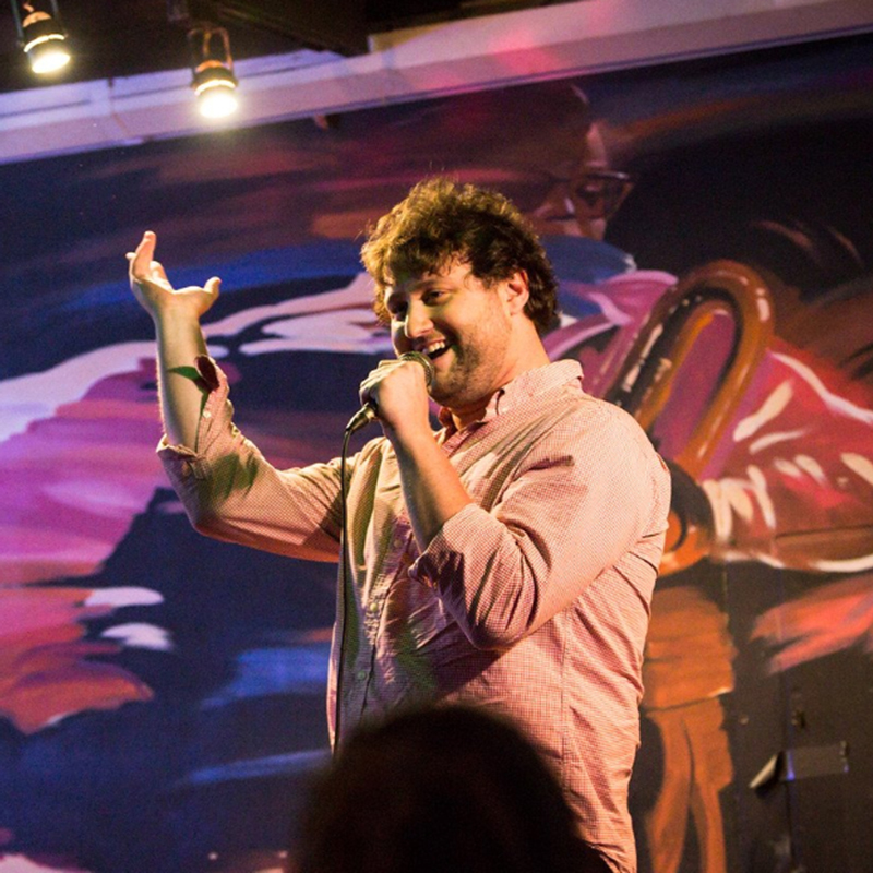 Comedian Mike Coletta performing on stage with microphone.