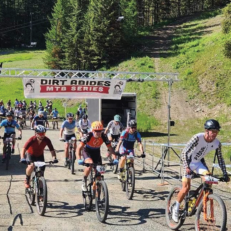 Start line of a cross country mountain bike races with numerous racers riding hard.