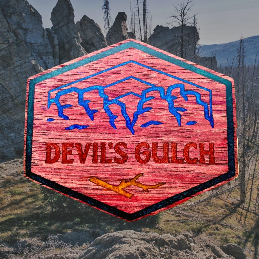 Image or 100 mile race winner belt buckle that says "Devils Gulch" on red background with outline of mountains above.