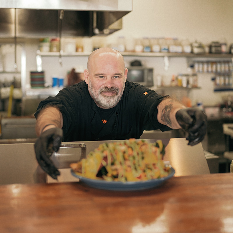 Line Cook serving plate of nachos with a smile.