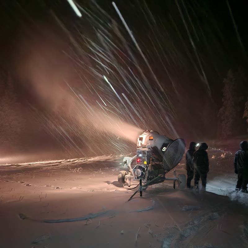 Snowgun making snow at night with snowmaker standing near by