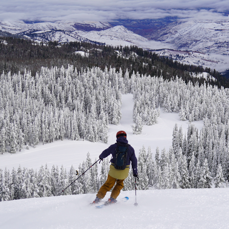 Skier descending Tumwater Ski Trail at Mission Ridge with view over Wenatchee Valley.