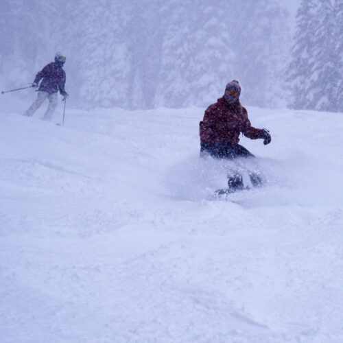 A snowboarder descending a ski trail at Mission Ridge on a powder day, spraying some snow in the air.