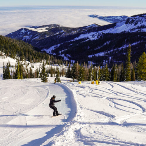 Snowboarder descending a groomed run at Mission Ridge, with view of clouds in the valley below.