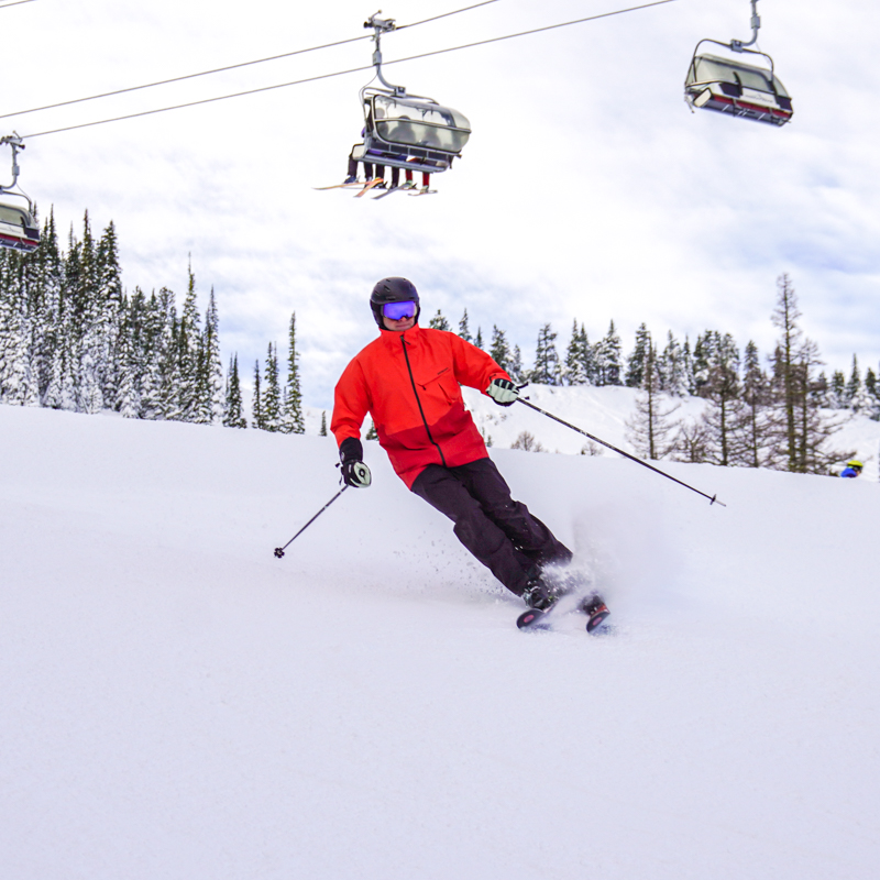 Skier in orange jacket descending Tumwater ski trail at Mission Ridge, with chairlift and trees in background.