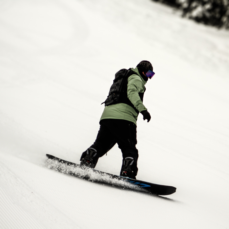 Snowboarder in green jacket carves fresh corduroy.