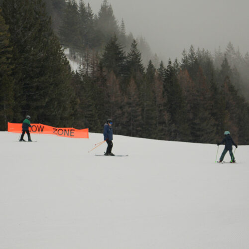 Two children learn to ski from a ski instructor in a wintery scene.