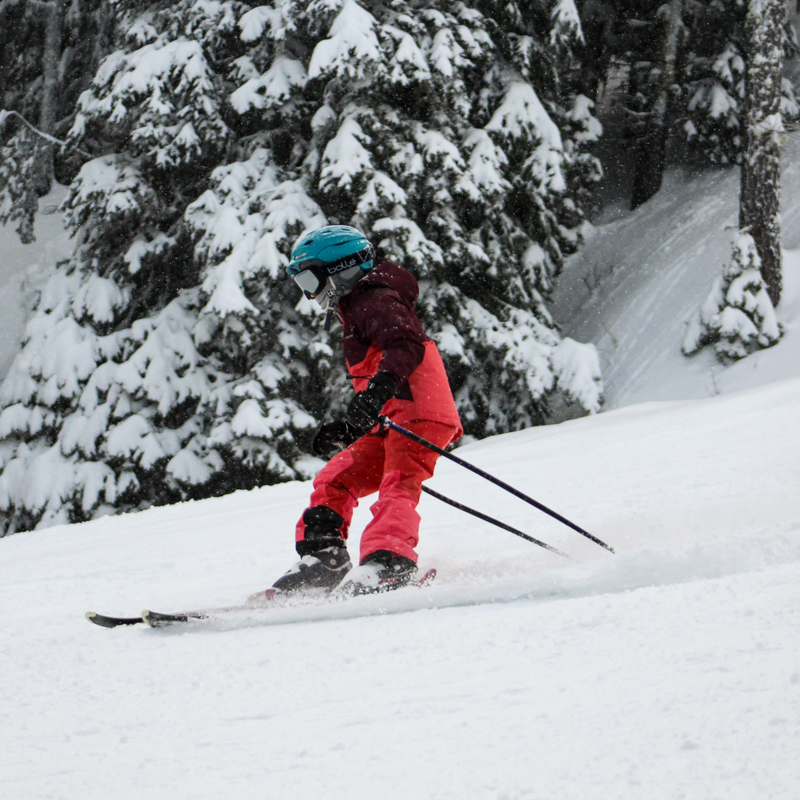 A child in a pink snowsuit skis downhill at Mission Ridge Resort