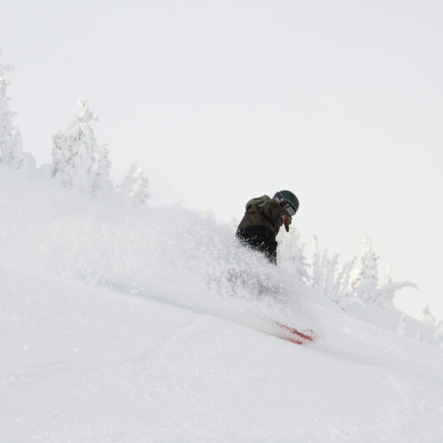 A snowboarder sends up a powder spray on a partly cloudy day.