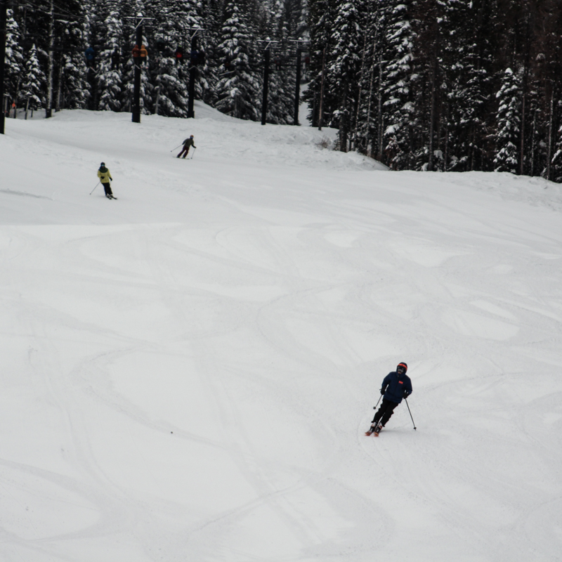 Three skiers descend the slope below a chairlift.