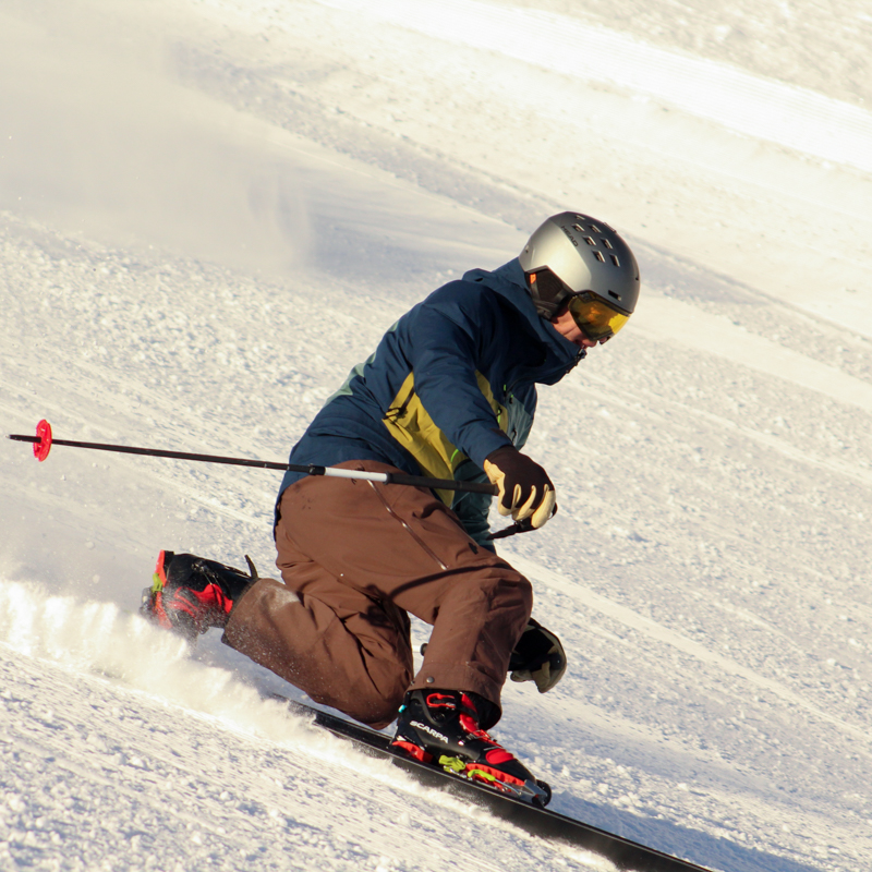 on a sunny day, a telemark skier carves a tight, steep turn.