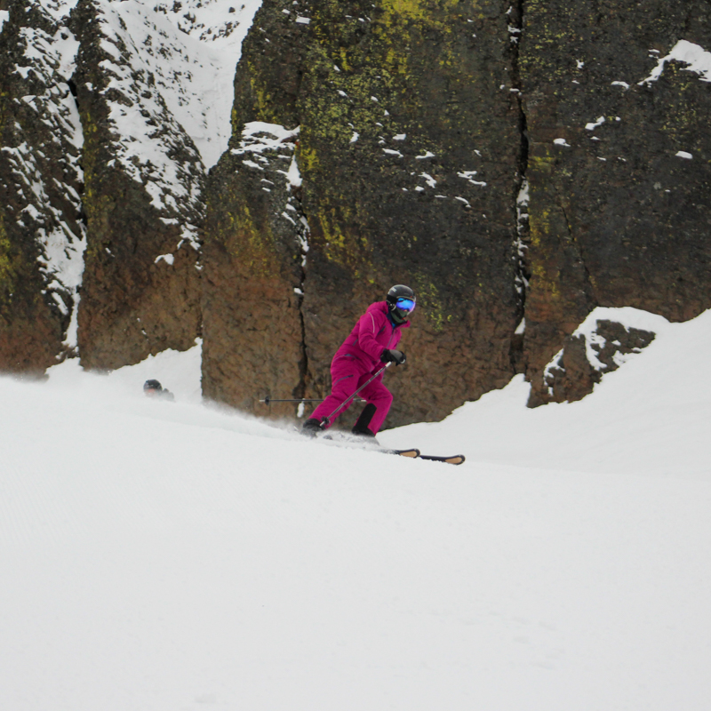 A young skier in pink crests a hill in front of basalt rock features.