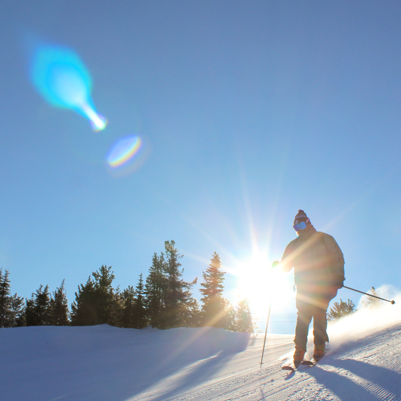 A sun flare eclipses a skier carving a groomed run