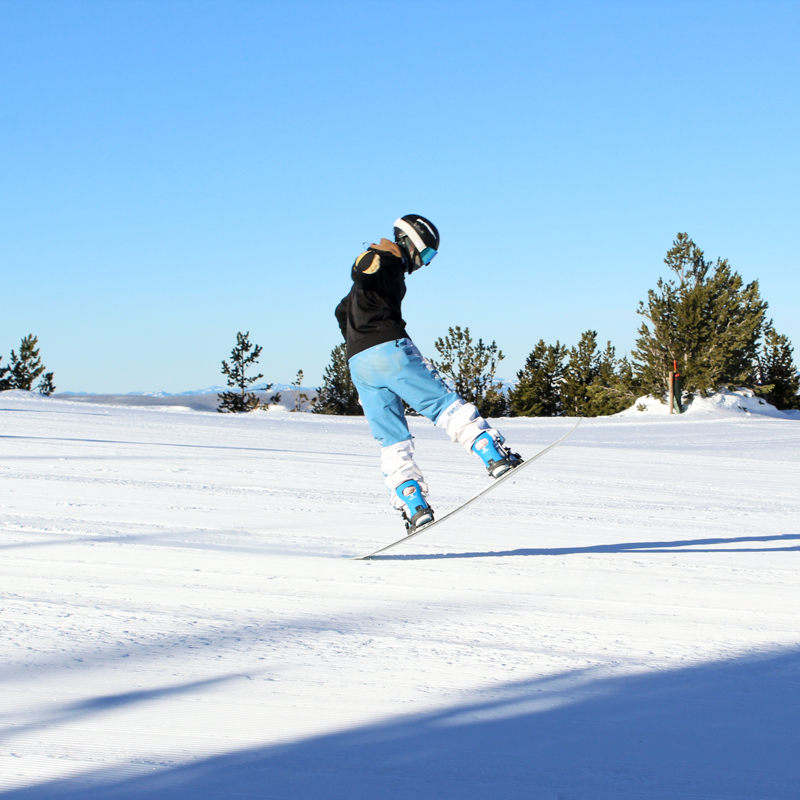 A child on a snowboard jumps and skims the tail of the board across corduroy on a sunny day