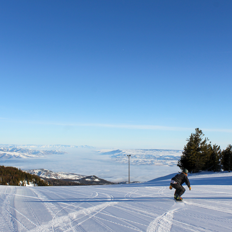 A snowboarder crouches low to the corduroy before dropping into a run over looking an inversion layer