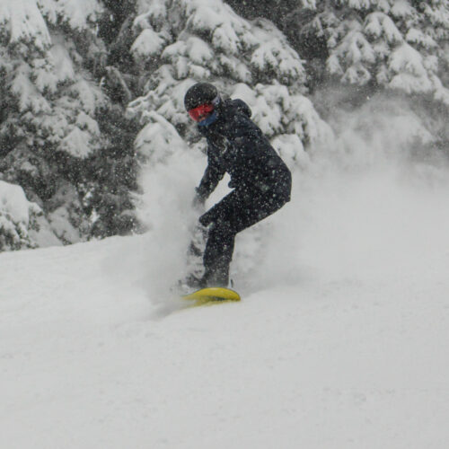 A young snowboarder sends a powder spray during a light snowfall.