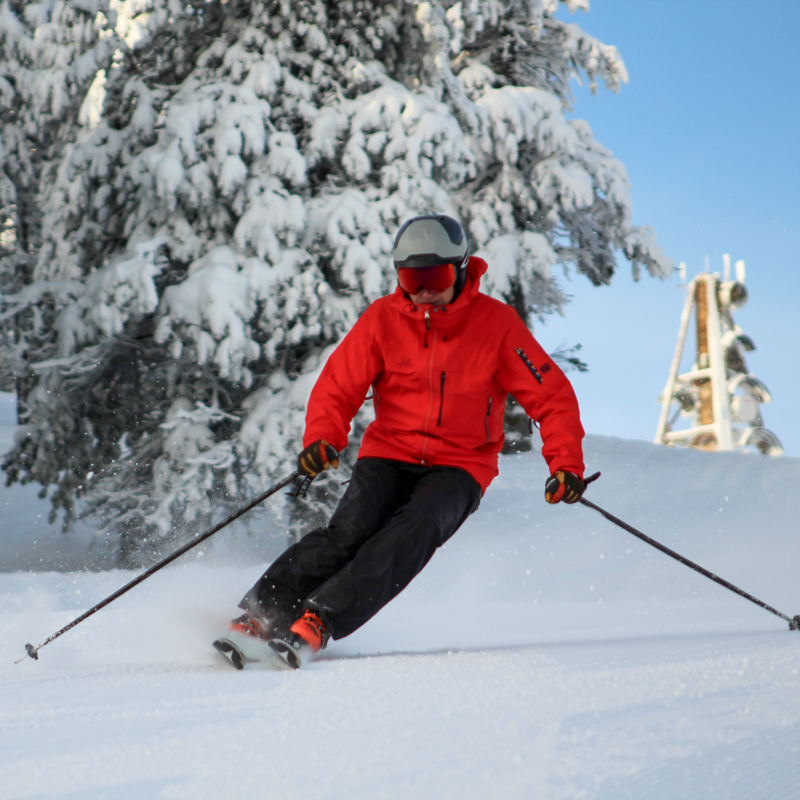 A skier in red carves on a sunny day.