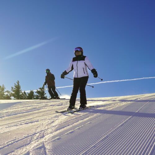 Two skiers descend the Sun Spot trail at Mission Ridge on a sunny morning with a freshly groomed surface.