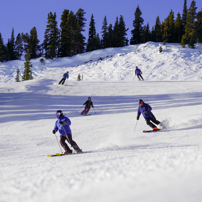 A group of skiers descends the Bomber Trail at Mission Ridge on a sunny day with a freshly groomed run.