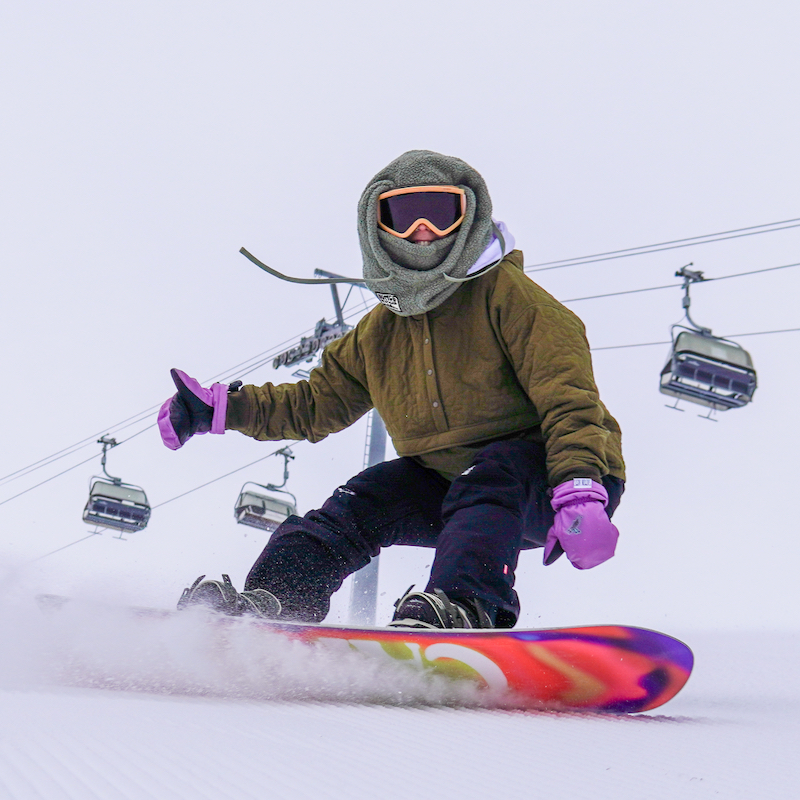 A snowboarder descends the Tumwater ski trail at Mission Ridge, with Chair 2 in the background.