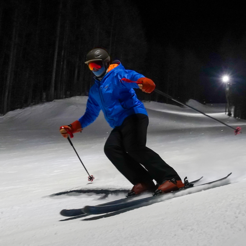 A skier descends the Tumwater trail at Mission Ridge in the night, with a light on in the background and an otherwise dark background.