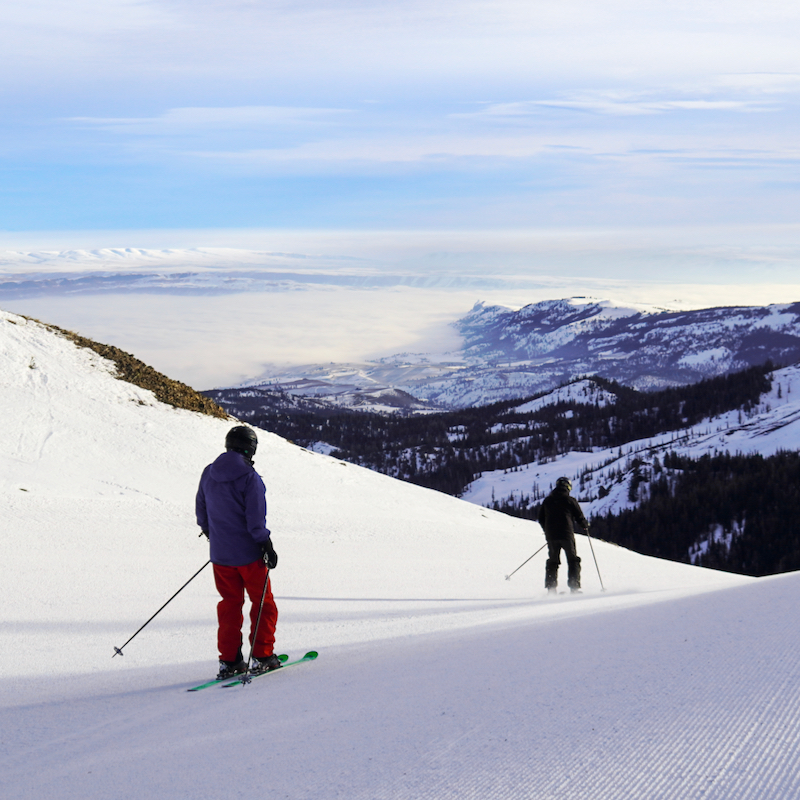 Two skiers descend the North Bomber Trail at Mission Ridge with a view into the Wenatchee Valley in the background.