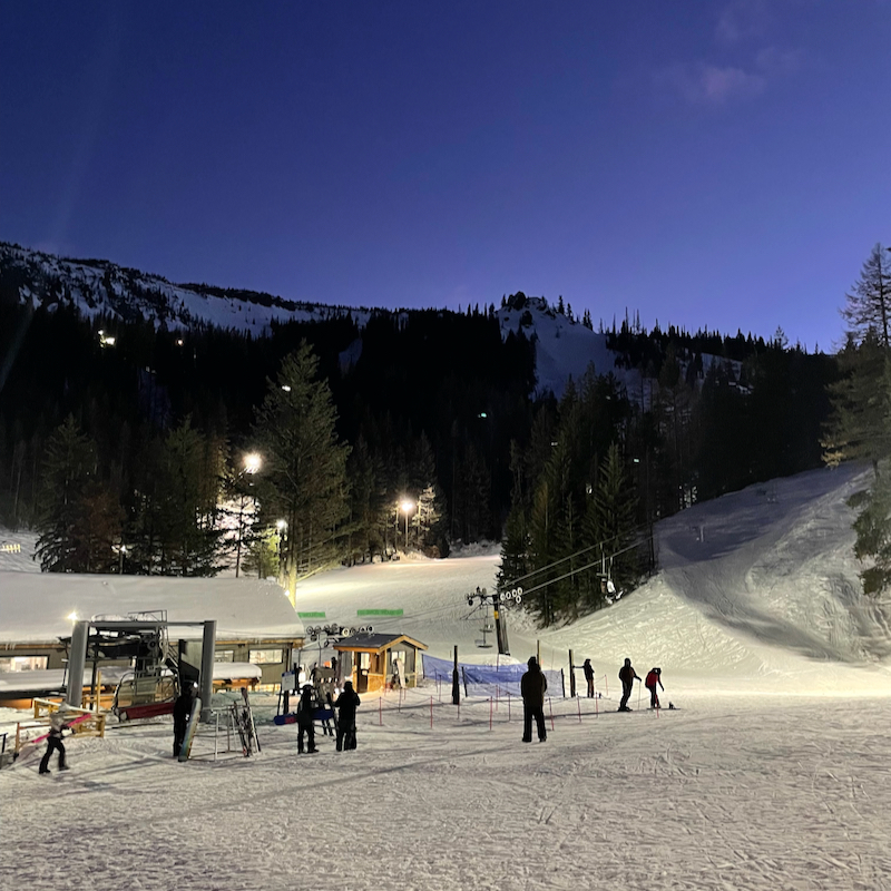 A view of the Mission Ridge base area in the evening, including snowy ground, the mountain behind, and the evening sky.