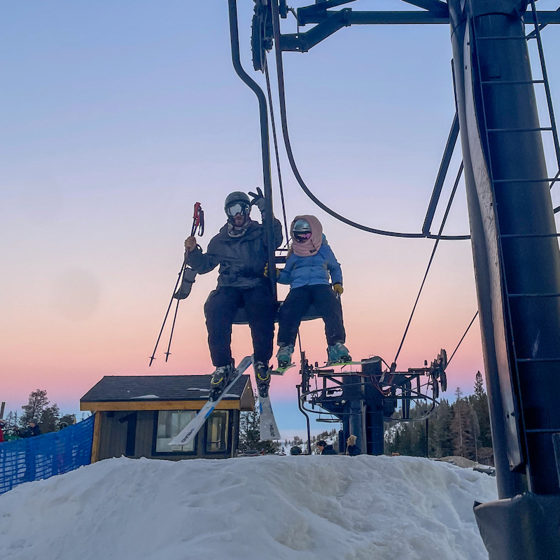 Two skiers ride Chairlift 1 at Mission Ridge with a pink sunset in the background.