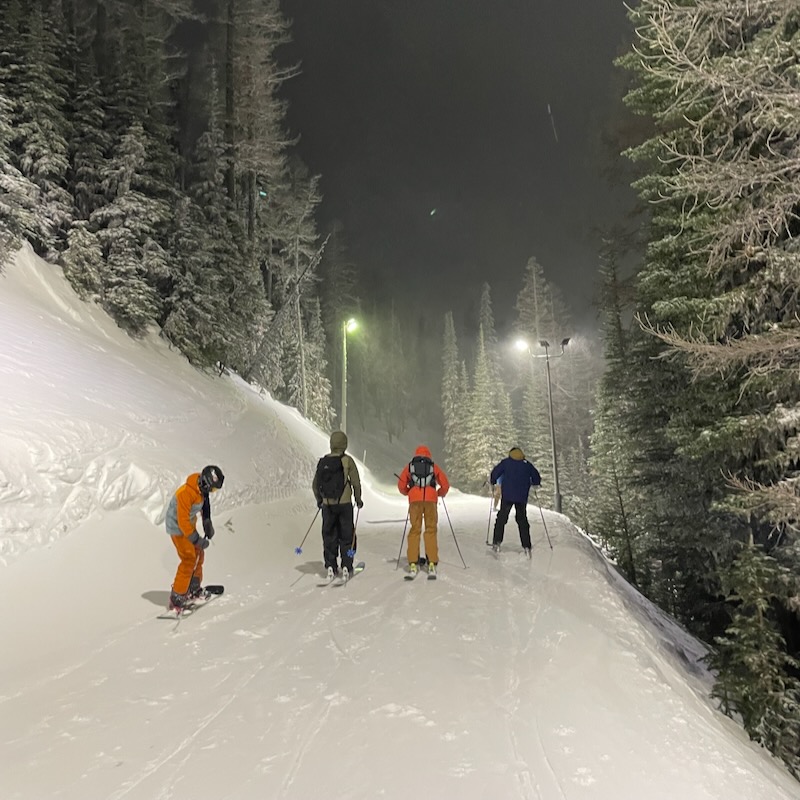 3 Skiers and a Snowboard traverse along a cat track at Mission Ridge during the night.