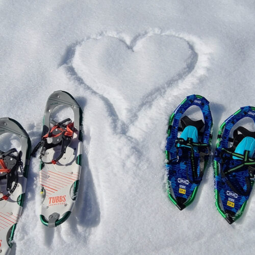 A heart drawn in the snow, flanked by 2 pairs of snowshoes.