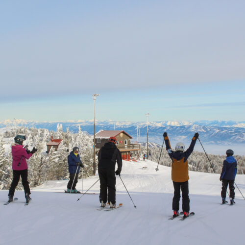 a group of skiers gather at the summit with the patrol shack and blue mountains in the background