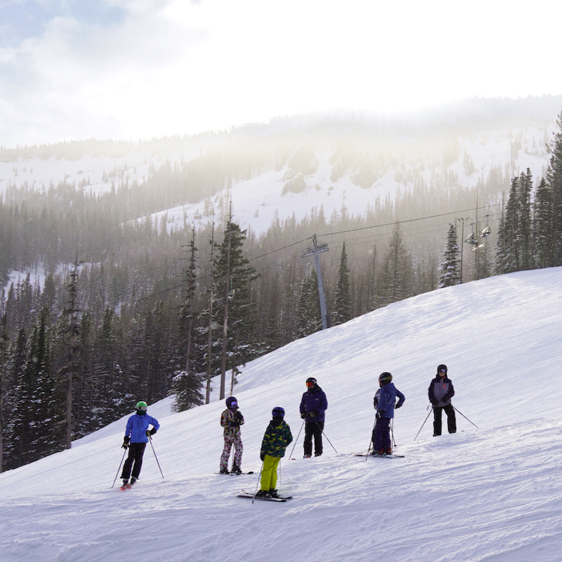 A group of skiers stands on the Bomber trail at Mission Ridge with a view of Wenatchee Mountain in the background.