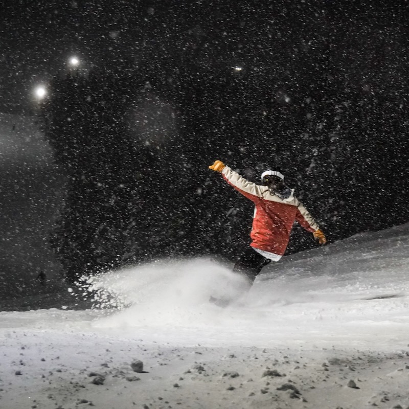 A snowboarder descends the sunspot trail at Mission Ridge at night while it's snowing.