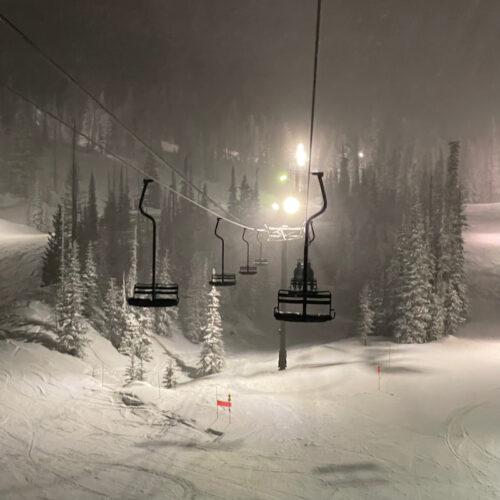 Chair 4 at Mission Ridge on a snowy night, with the lights on illuminating the snow covered evergreen trees.