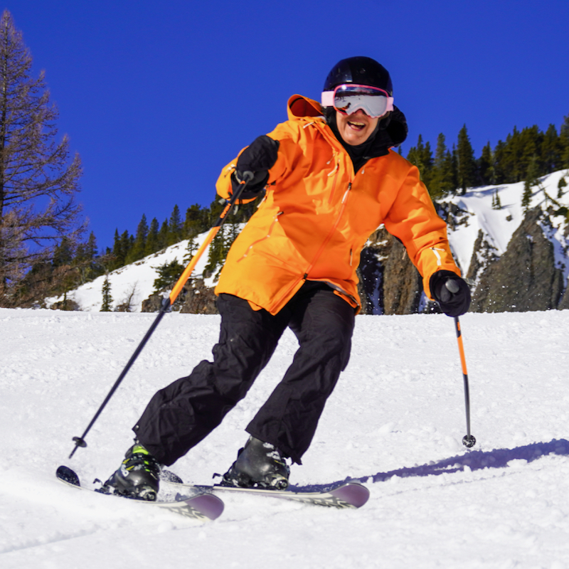 A skier in an orange jacket descends the Hidden Valley Trail at Mission Ridge, with the Bomber Cliffs in the background.