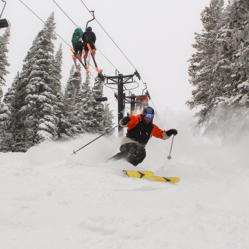 a male skier sprays powder beneath a chair lift