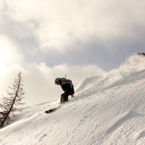 a child skis off piste on a bluebird morning