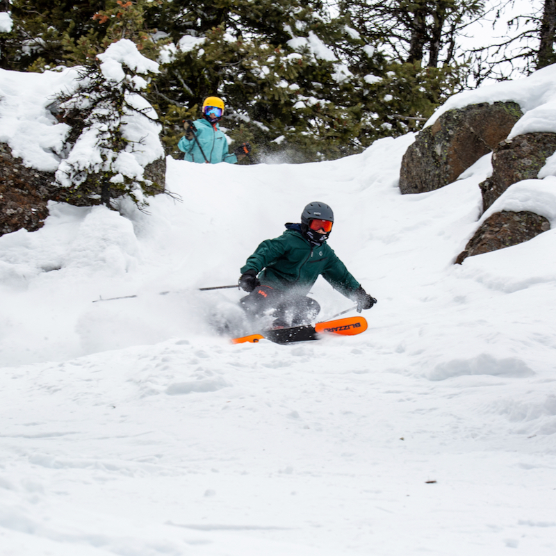 A skier descends a chute at Mission Ridge, with another skier watching on in the background.