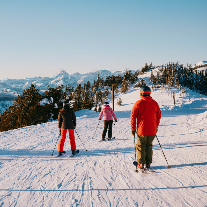 Skiers on the Boundary Road at Mission Ridge in the afternoon with blue skies and a view of snowy Mt. Stuart in the background.